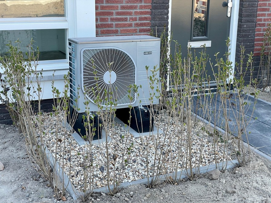 Außeneinheit einer Luft-Wasser-Wärmepumpe vor einem Wohnhaus, installiert im Gartenbereich neben der Hauswand.